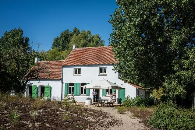 Het witte Vanneuvillehuis met groene luiken tussen het groen.